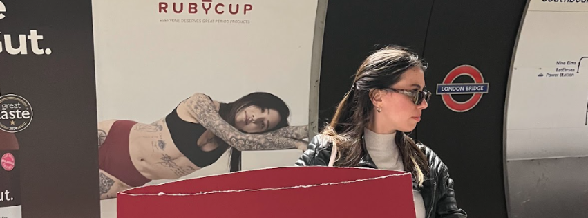 woman holding a sign in front of Ruby Cup advert in London tube