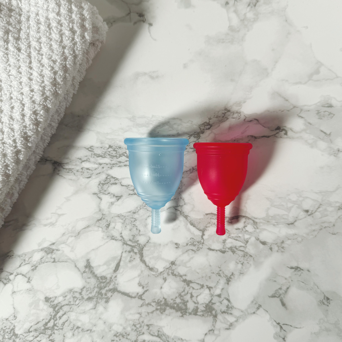 Blue and red Ruby Cup menstrual cups on a marble surface with a towel.