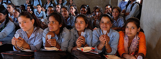 Children sitting at a table in a classroom setting, holding a Ruby Cup menstrual cup