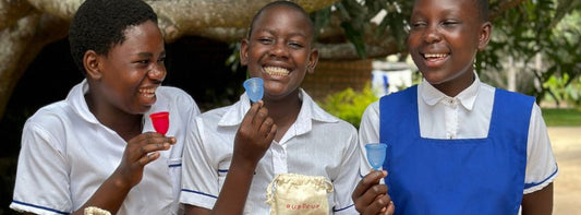 Three schoolchildren in uniforms holding Ruby Cup menstrual cups