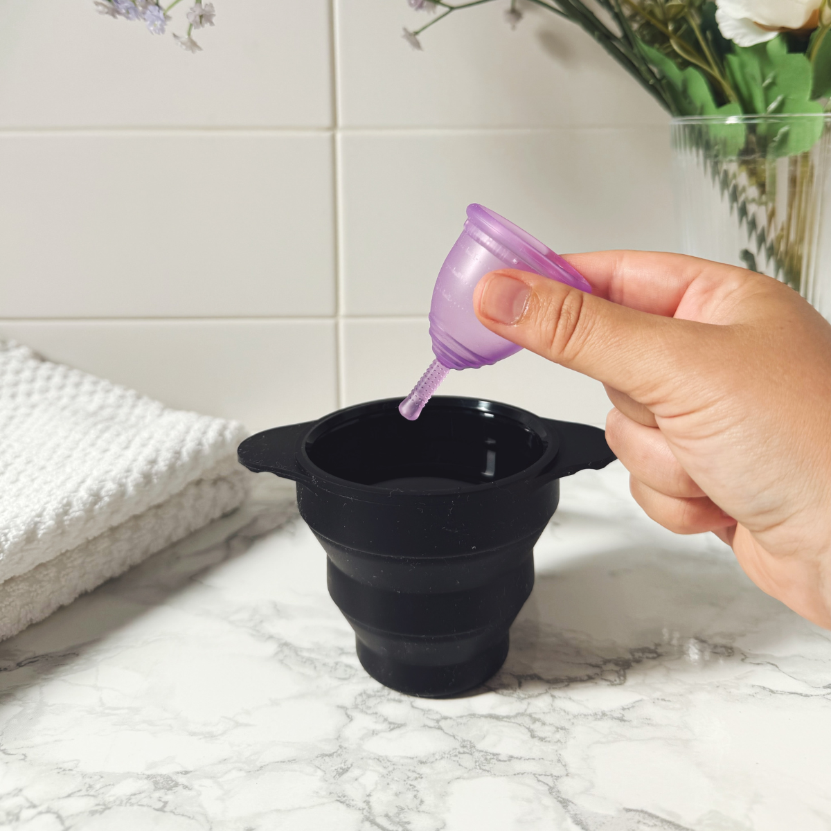 Person placing a purple Ruby Cup menstrual cup into a black steriliser on a marble surface