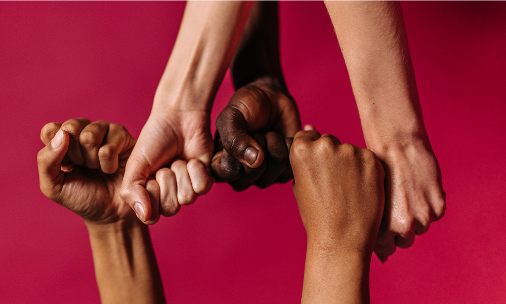 Four hands of different skin tones interlocked against a red background